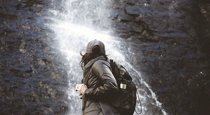 woman wearing an anello backpack standing near waterfall