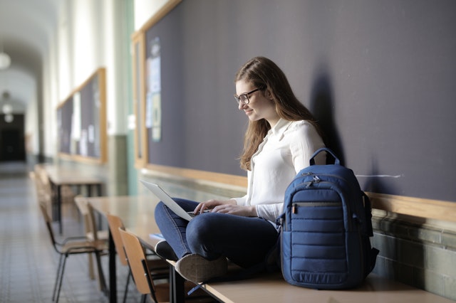 woman using laptop next to a blue backpack