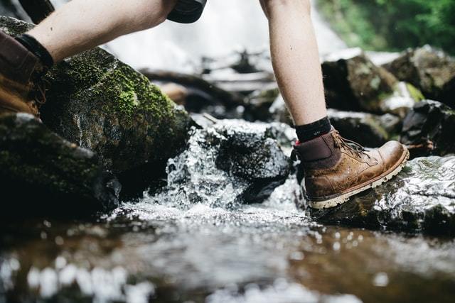 person walking through stream wearing boots