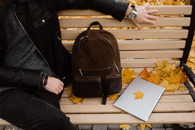 person sitting on a bench with a leather backpack and laptop